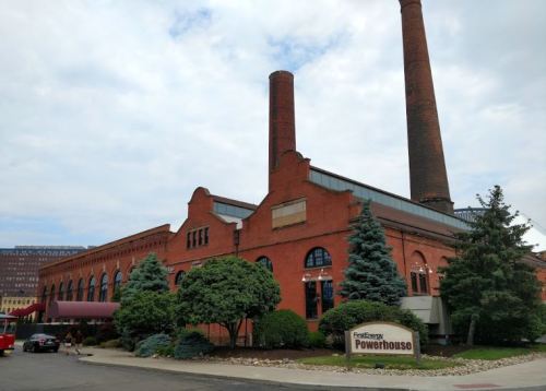 Historic red brick building with tall smokestacks, surrounded by trees and a sign reading "FirstEnergy Powerhouse."