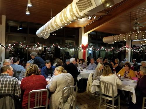 A festive dining scene with people enjoying a meal, decorated with holiday lights and a warm atmosphere.