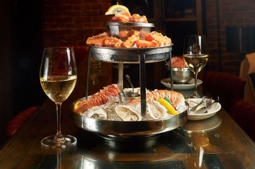 A seafood tower featuring oysters and lobster, accompanied by white wine in a glass, set on a wooden table.