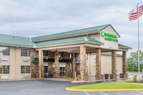 Exterior view of a hotel with a green roof, stone pillars, and flags, set against a cloudy sky.