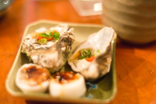 A plate with two oysters topped with green onions and sauce, set on a wooden table.