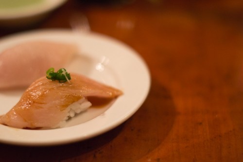 A close-up of two pieces of sushi on a white plate, garnished with green onion, on a wooden table.
