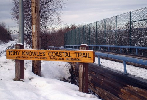 Sign for Tony Knowles Coastal Trail in Anchorage, surrounded by snow and a fence in the background.