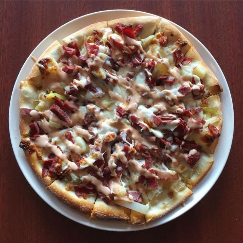 A round pizza topped with bacon, onions, and drizzled with a creamy sauce on a wooden table.