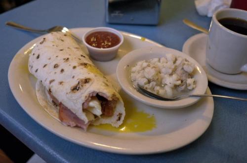 A plate with a rolled tortilla filled with ham and cheese, served with salsa and a side of cottage cheese, next to a coffee cup.