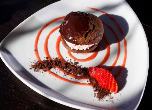 A chocolate dessert with a creamy filling, drizzled with strawberry sauce and garnished with a fresh strawberry.