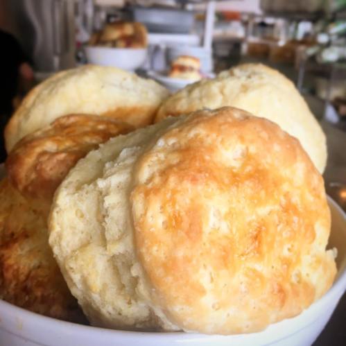 A close-up of golden, flaky biscuits stacked in a bowl, showcasing their fluffy texture and appetizing appearance.