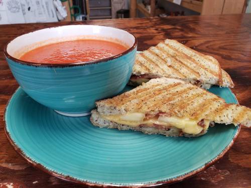 A bowl of tomato soup next to a grilled cheese sandwich on a turquoise plate, set on a wooden table.