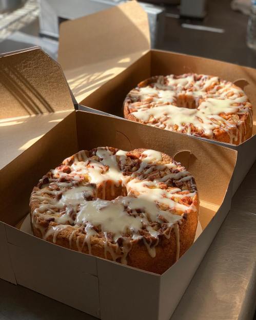 Two round cakes with icing, placed in open cardboard boxes, sitting on a table with soft lighting.