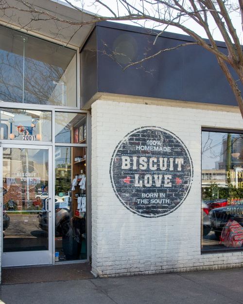 Exterior of a restaurant with a sign reading "100% Homemade Biscuit Love - Born in the South" on a white brick wall.