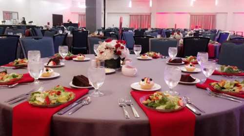 A banquet table set with salads, desserts, and drinks, surrounded by empty chairs in a decorated dining hall.