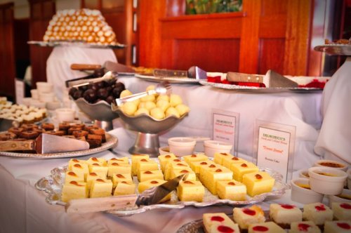 A variety of desserts displayed on silver trays, including cakes, chocolates, and sweets, set on a white tablecloth.