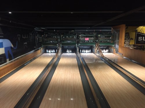 A view of two bowling lanes with pins set up at the end, illuminated under dim lighting.