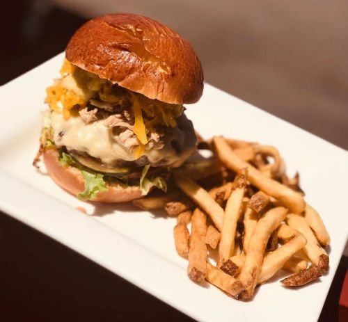 A delicious burger with melted cheese, pulled pork, and toppings, served with a side of crispy French fries.