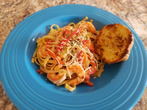 A blue plate with shrimp pasta topped with cheese and herbs, accompanied by a slice of toasted garlic bread.