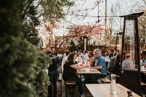 A lively outdoor dining scene with people enjoying meals and drinks at long tables under string lights.