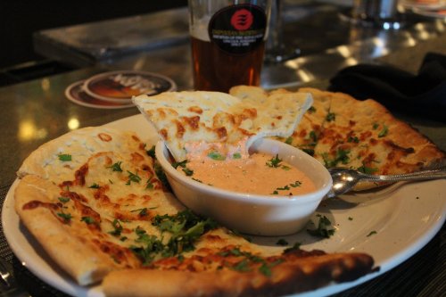A plate of naan bread with a bowl of dipping sauce, garnished with herbs, alongside a glass of beer.