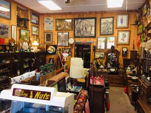 A cozy antique shop filled with vintage items, framed art, and nostalgic decor on wooden walls.