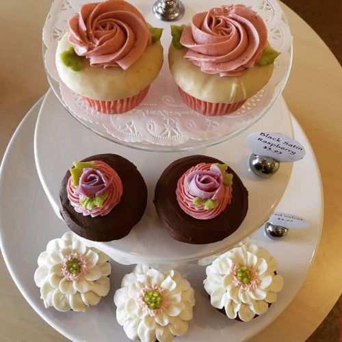 A tiered display of colorful cupcakes with floral decorations, including pink and white frosting, on a white plate.