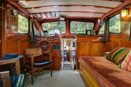 Cozy interior of a wooden boat, featuring a steering wheel, seating area, and small sleeping quarters.
