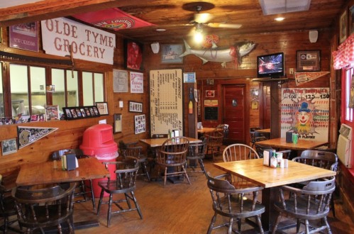Cozy restaurant interior with wooden walls, tables, and vintage decor, featuring a TV and various memorabilia.