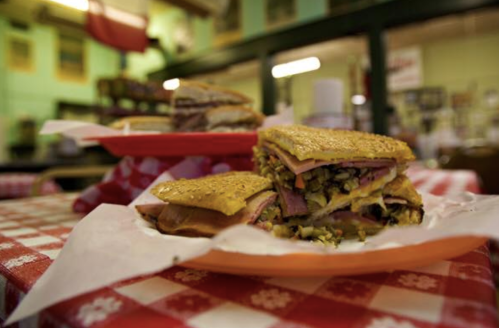 A close-up of a layered sandwich on a red and white checkered tablecloth, with another sandwich in the background.