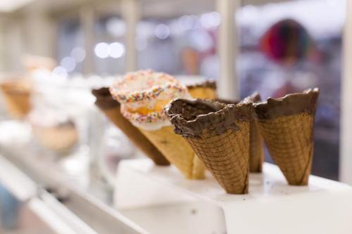 A display of ice cream cones, including chocolate-dipped and sprinkles, on a counter in a bright shop.