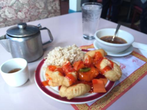 A plate of sweet and sour chicken with rice, a bowl of soup, a teapot, and a glass of water on a table.