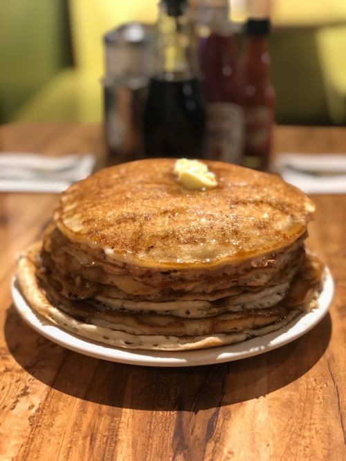 A tall stack of golden pancakes topped with a pat of butter, served on a white plate on a wooden table.