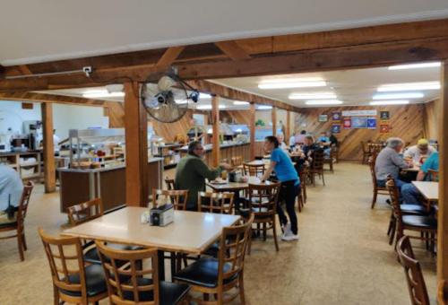 A cozy restaurant interior with wooden decor, tables occupied by diners, and a buffet area in the background.