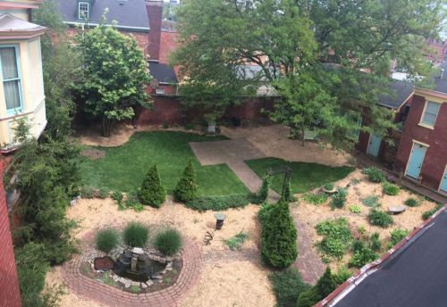 Aerial view of a landscaped courtyard with grass, trees, and a stone pathway surrounded by brick buildings.