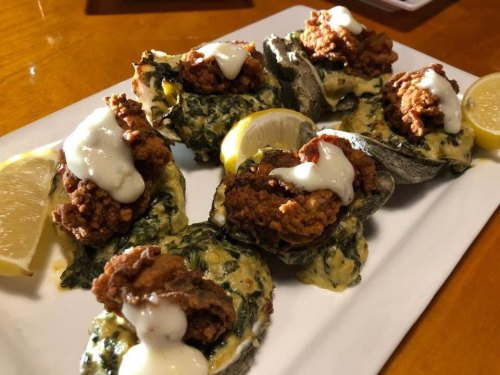 A plate of baked oysters topped with fried chicken, creamy sauce, and lemon wedges.