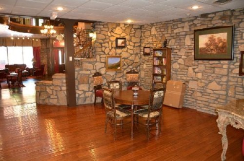 Cozy interior featuring a stone wall, wooden floors, a dining table, and a bookshelf in a warm, inviting space.