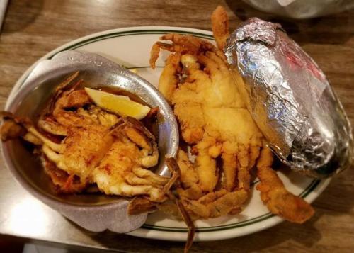 A plate featuring fried crab, a lemon wedge, and a baked potato wrapped in foil.