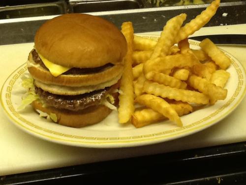 A plate with a stacked burger topped with cheese and lettuce, accompanied by a side of crinkle-cut fries.
