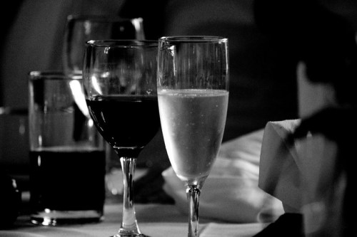 Two elegant glasses on a table: one filled with red wine and the other with sparkling champagne, in black and white.