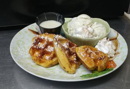 A plate with waffles, a small cup of syrup, and a bowl of ice cream topped with whipped cream and cinnamon.