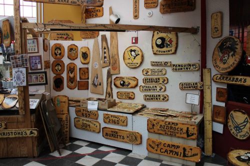 A display of wooden signs and plaques with various designs and names, arranged on a wall in a shop.