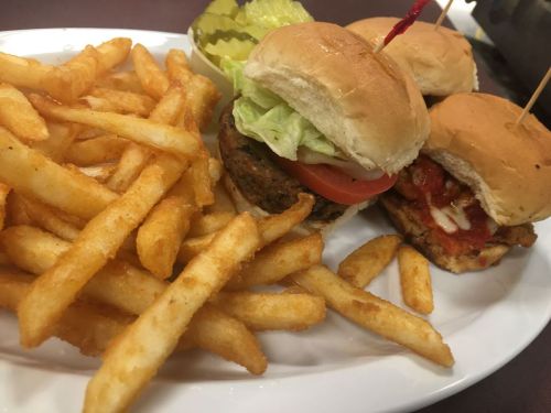 A plate with three mini burgers topped with lettuce and tomato, served with a side of crispy French fries and pickles.