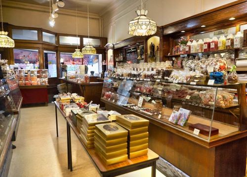 A charming candy shop interior with glass displays filled with sweets and chocolates, warmly lit by vintage lamps.