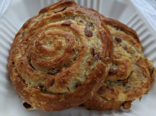 Two golden-brown spiral pastries with a flaky texture, placed on a white paper plate.