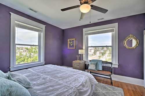 Cozy bedroom with purple walls, a large bed, windows, a mirror, and a small bench by the window.
