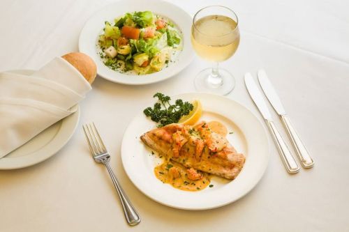 A plate of grilled fish with sauce, garnished with lemon, alongside a fresh salad and a glass of white wine.