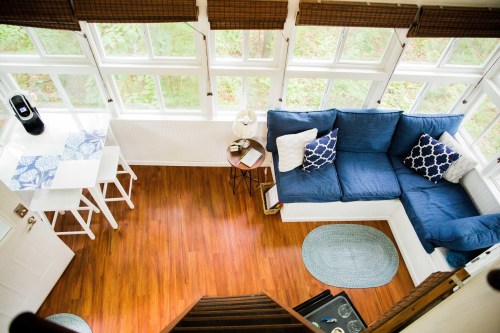 Cozy living space with a blue sectional sofa, small dining table, and large windows overlooking greenery.