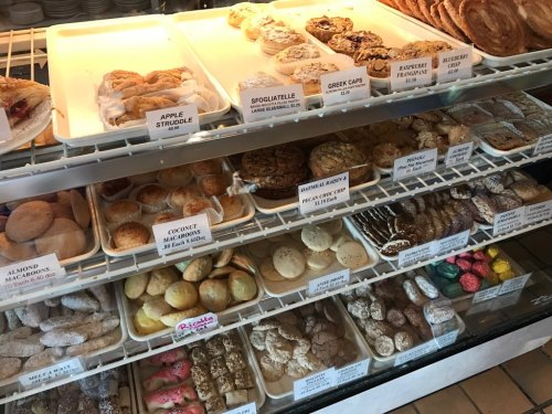 A display case filled with various baked goods, including pastries, cookies, and strudels, labeled with prices.