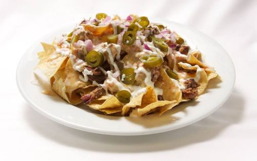 A plate of nachos topped with beef, jalapeños, onions, and drizzled with sour cream.