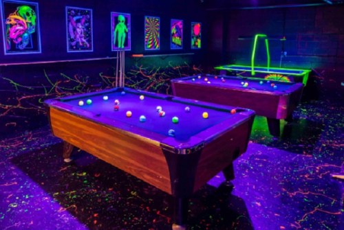 A vibrant pool hall with glowing tables, neon artwork, and colorful balls under blacklight.