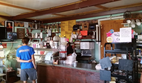 A person stands at a counter in a cozy café, surrounded by colorful menus and various food items.