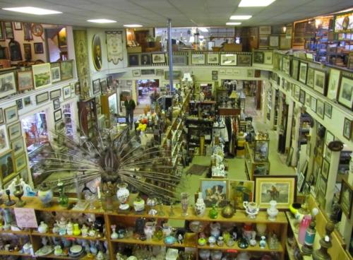 A spacious antique shop filled with various collectibles, framed art, and decorative items on shelves and walls.