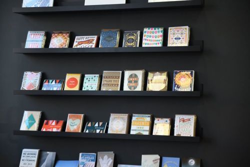A display of colorful greeting cards arranged on black shelves against a wall.